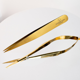 Gold tweezers with 'Suzanne Egan' branding on a light gray background